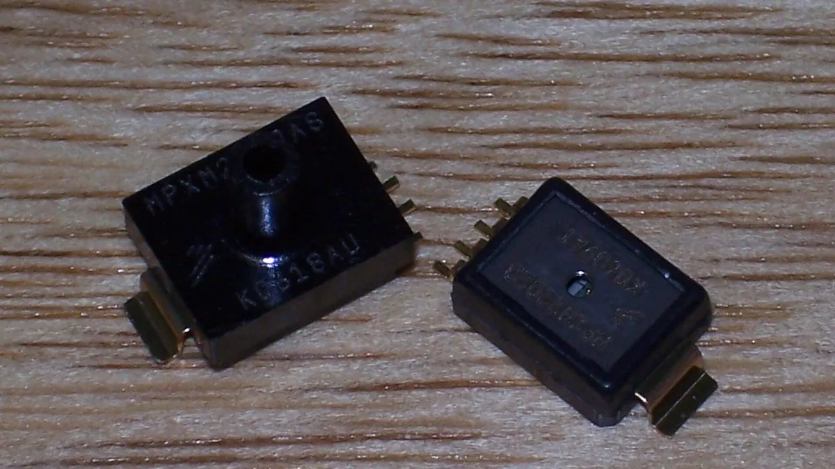 Two small black pressure sensor IC packages on a wooden surface