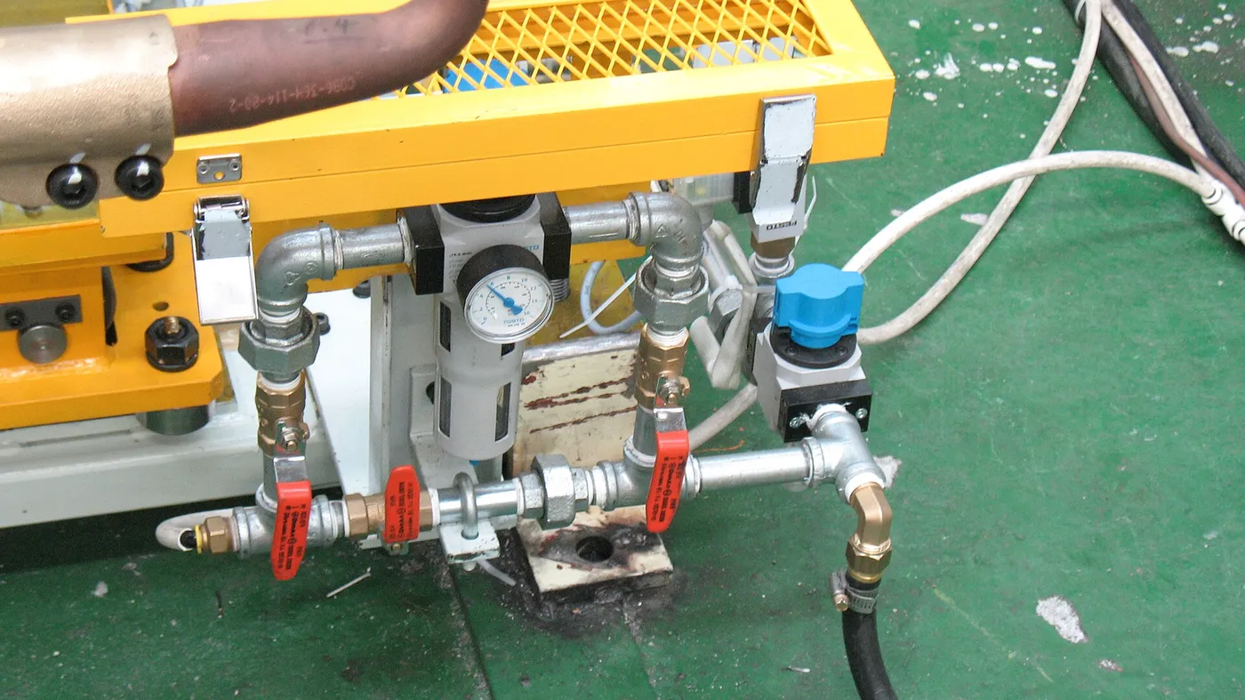 Industrial piping and valves with a yellow control panel on a plant floor